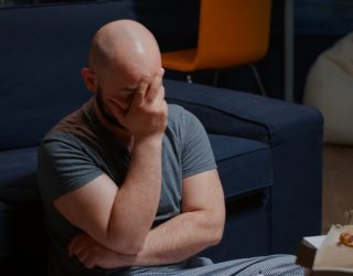 Shocked man sitting on floor at home reading bad news holding documents paper letter feeling desperate about financial problems, domestic bills. Person overwhelmed by tragedies that happened